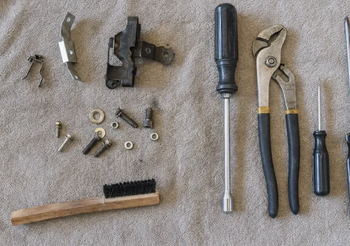 Two oven-door hinge assemblies on a canvas cloth with tongue-and-groove pliers, a screwdriver and washers