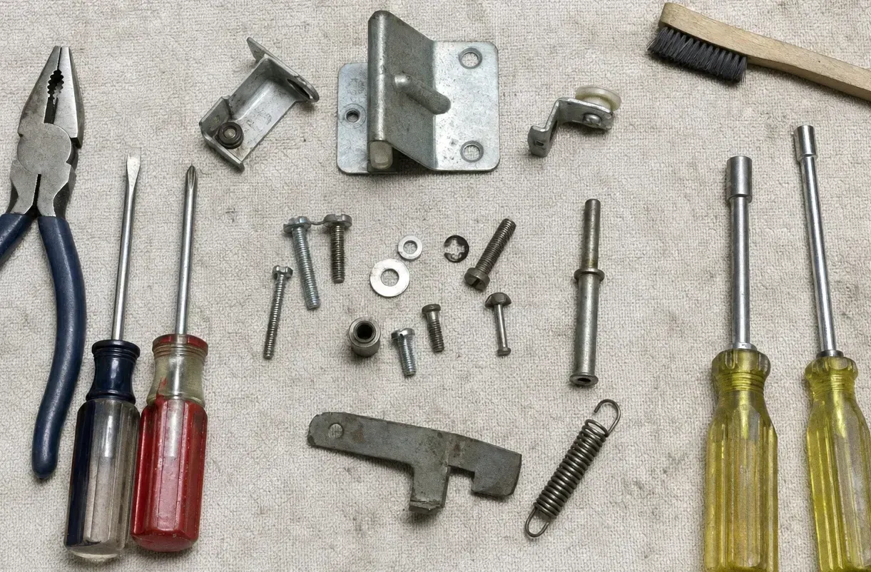 Hinge plates, a coil tension spring and a latch arm set out on a canvas cloth with a red-handled screwdriver